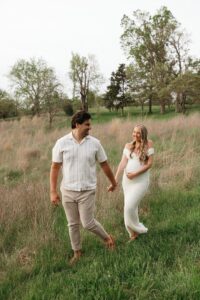 candid maternity photo of couple laughing together in grassy field at Queeny Park St. Louis