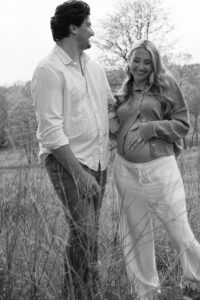 candid maternity photo of couple laughing together in grassy field at Queeny Park St. Louis